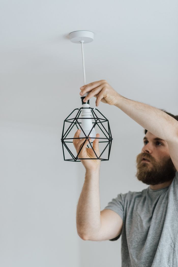 menu-02 Concentrated repairman screwing light bulb in stylish lamp hanging on ceiling of new flat